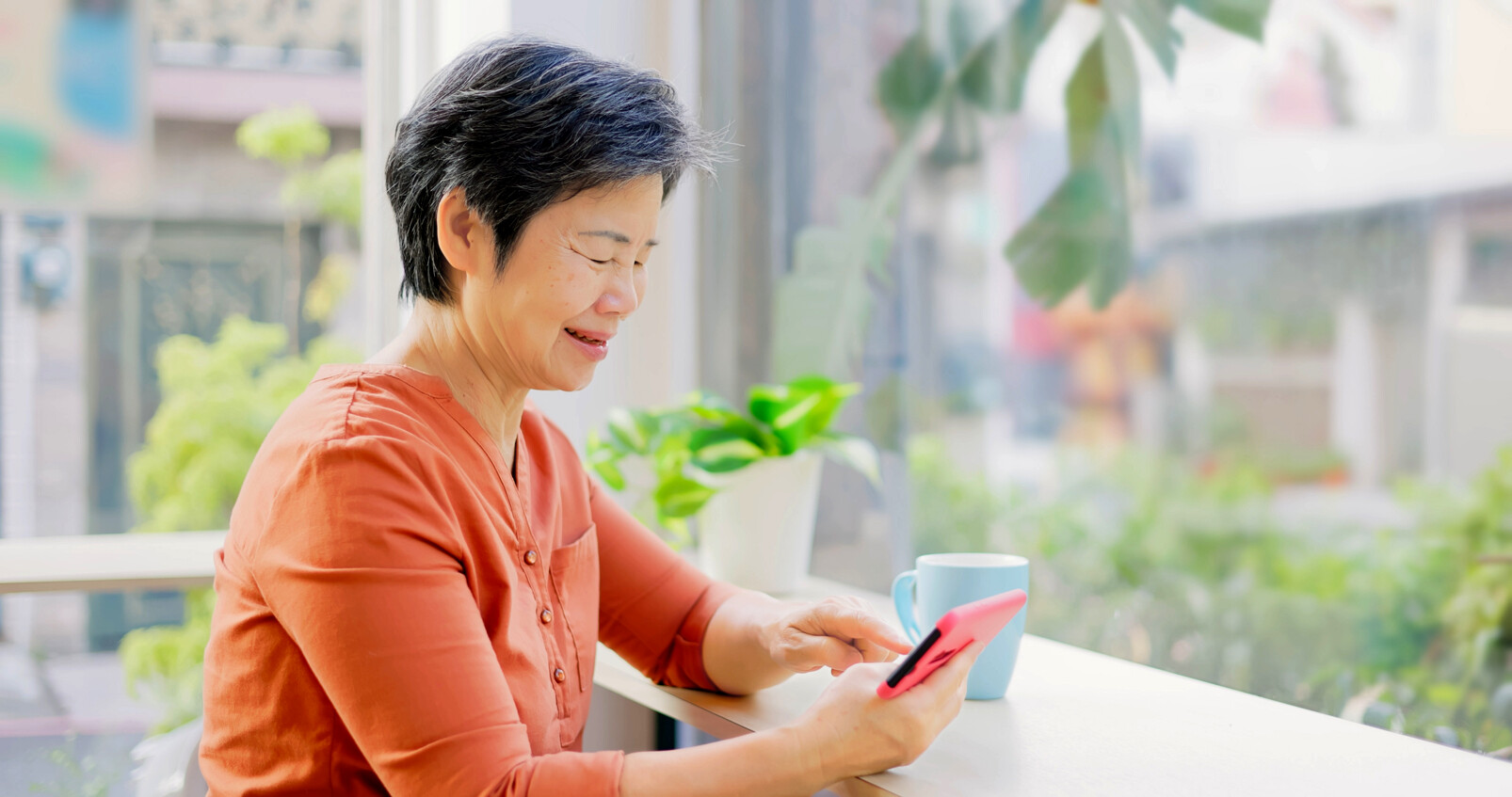 Happy Old Woman With Mobile Phone Watching Video In The Coffee Shop